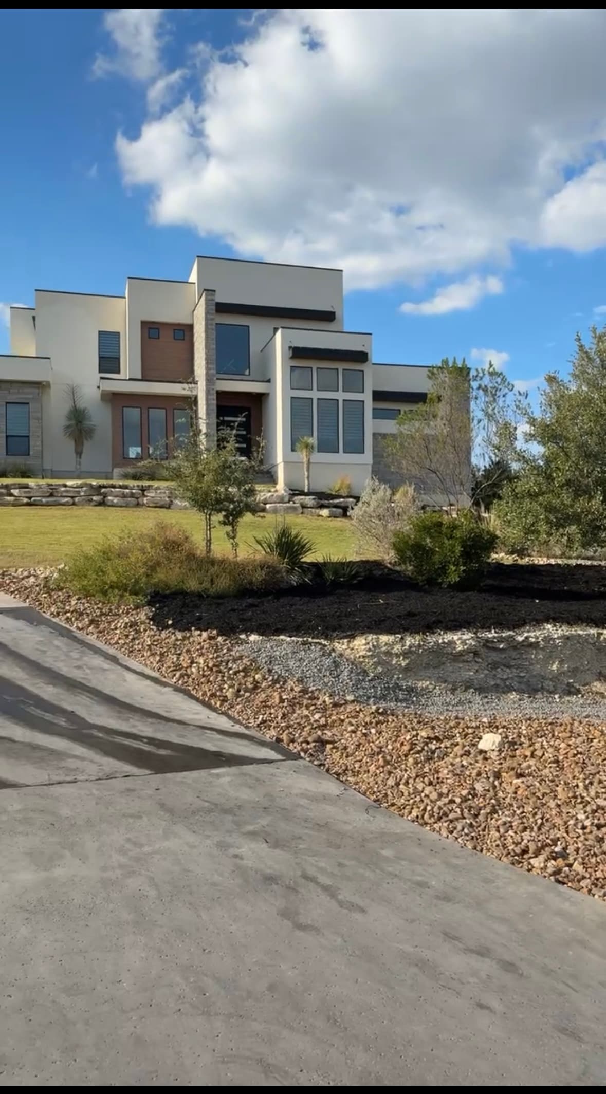 Modern white house with wood accents and large windows overlooking a tiered landscaped front yard.