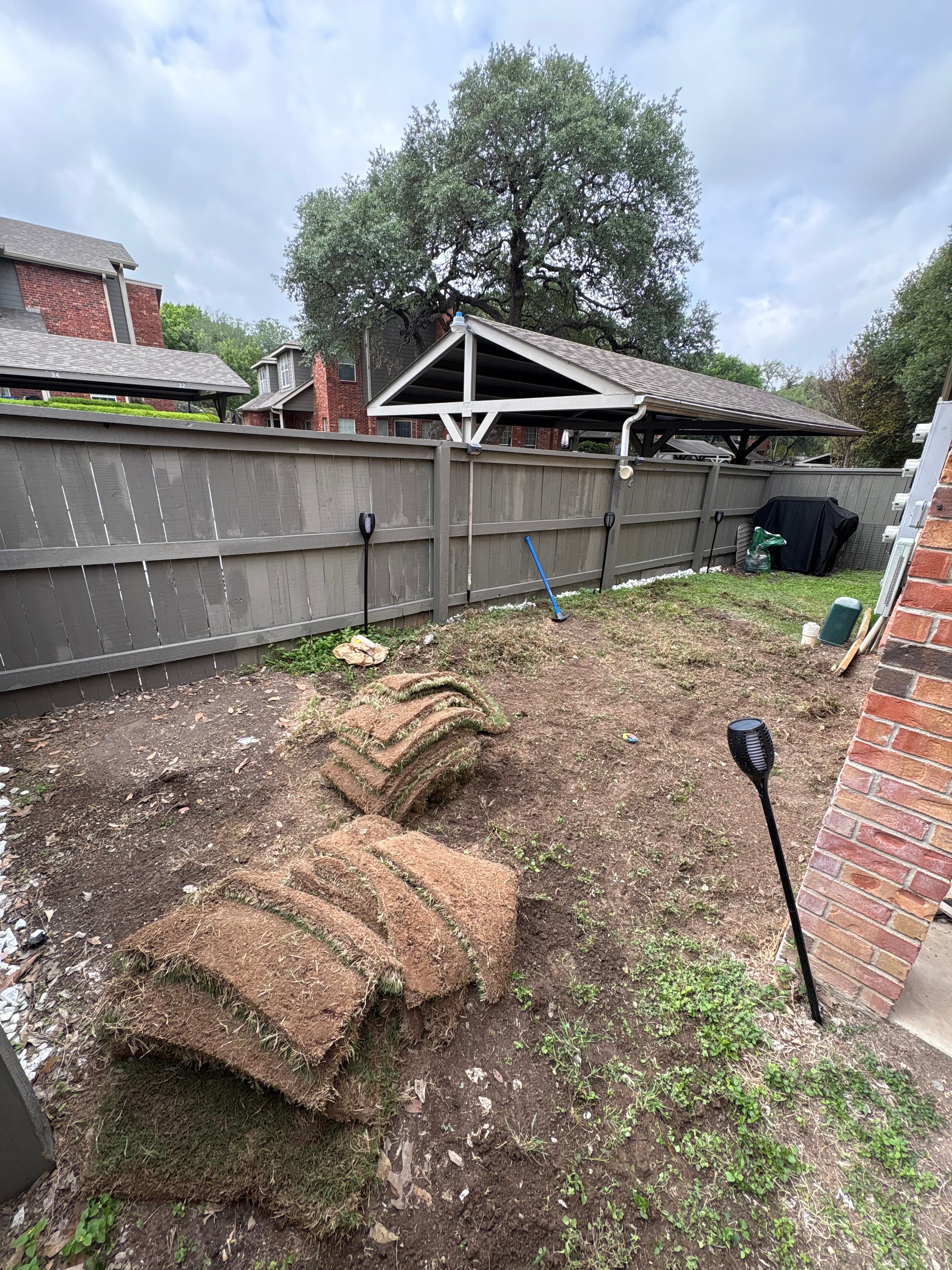 Stacks of new grass sod on bare dirt in a backyard landscaping project.